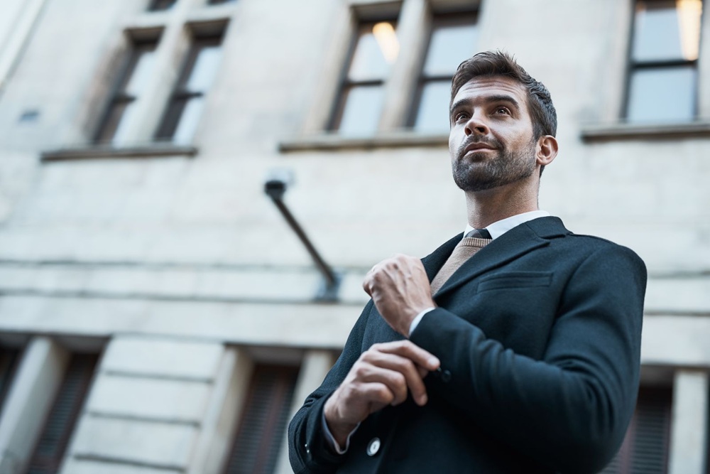 job fair attire A man in a suit stands outdoors in front of a stone building, looking slightly upward with a confident expression.