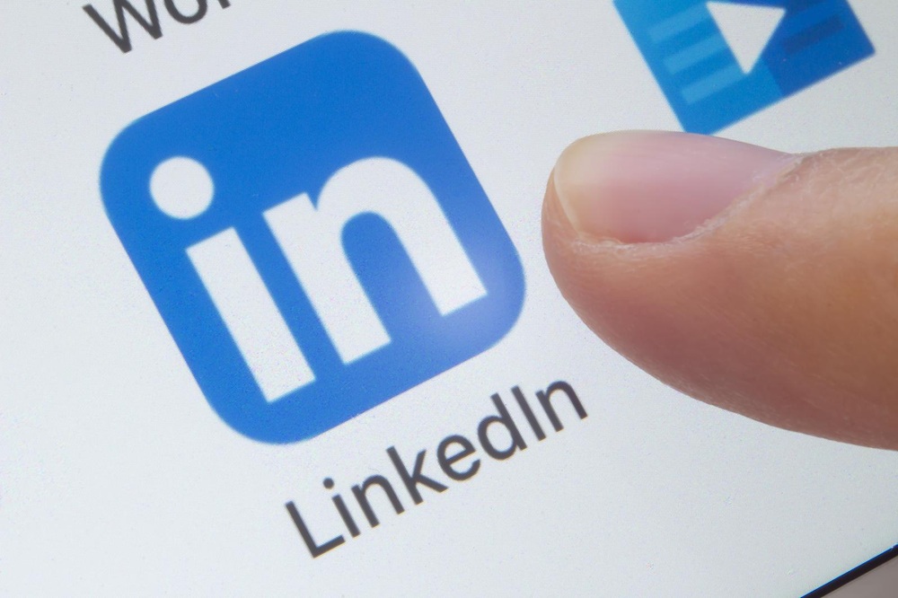A finger about to tap the LinkedIn app icon on a touchscreen device, ready to explore LinkedIn jobs in Charlotte, NC.